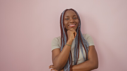 Confident african woman with braids posing against a pink background, her cheerful demeanor...