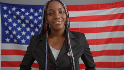 Confident african american woman with braids wearing a blazer poses in an office with the usa flag.