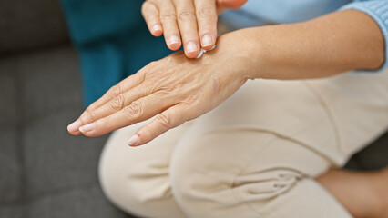 A hispanic woman applies cream to her hands at home, signaling self-care and wellness in an indoor setting.