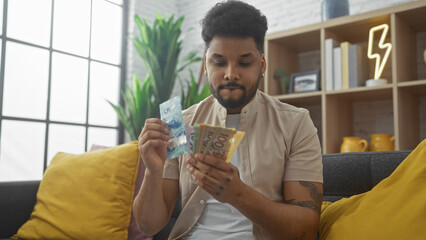 Handsome man counting canadian dollars in a cozy living room setting
