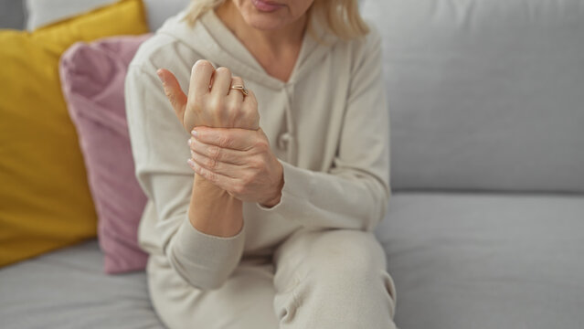 A caucasian woman experiencing wrist pain at home, sitting on a sofa with colorful pillows in a cozy living room setting.