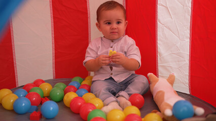 Fototapeta na wymiar Adorable toddler playing with toys sitting inside of circus tent at home