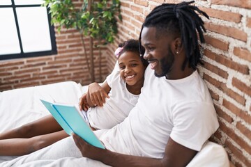 Father and daughter reading book sitting on bed at bedroom