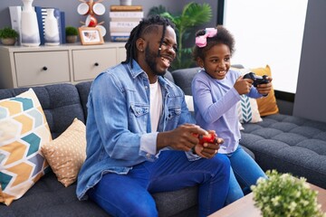 Father and daughter playing video game sitting on sofa at home