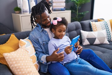Father and daughter watching video on touchpad sitting on sofa at home