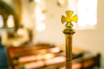 Shallow focus of a golden cross seen in the warm light of an English church. The alter is located...