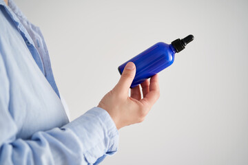 Female hands in a blue shirt hold a blue bottle of serum.