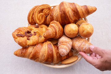 Sweet baked goods and croissants in the basket, woman's hands take a creamy croissant with sugar