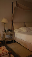 An elegant bedroom features a canopy bed, lamp, phone, and comfortable bedding conveying a sense of luxury hospitality.