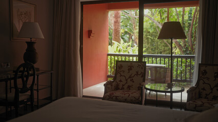 A tranquil hotel room with a comfortable bed, elegant furniture, inviting balcony, and a view of lush greenery.