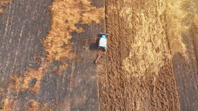 From above, a tractor carves intricate patterns on arid soil, a cloud of dust following its every move. The landscape, once golden-brown, now bears the mark of human endeavor.
