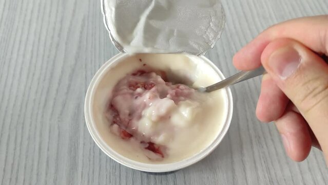 Man stirs pudding with rice and strawberries in a plastic cup with a spoon. First person view