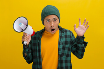 Excited Asian man in a beanie hat and casual shirt holding a megaphone announces a discount sale...