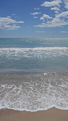 Serene beach scene with glistening waves, clear sky, fluffy clouds, sunshine, ocean, sand,...