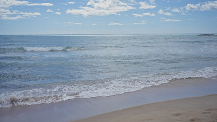 Serene beachscape with clear skies, gentle waves, and an inviting sandy shore under bright daylight.