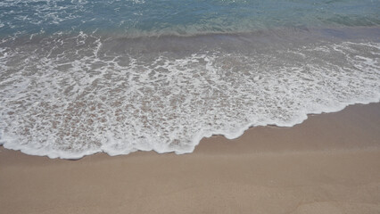 Waves gently caress the sandy shore under a clear sky, conveying serenity and natural beauty.
