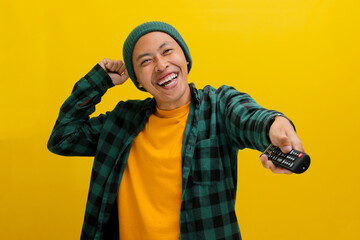 Excited Asian man, dressed in a beanie hat and casual shirt, watches a TV show or movie, pressing a...