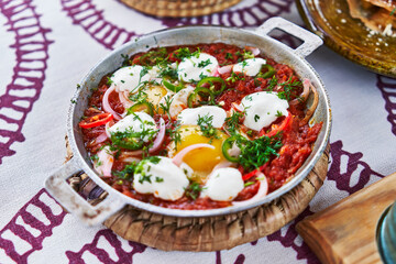 Traditional shakshuka in a pan adorned with poached eggs, tomatoes, onions, and parsley, ready for...