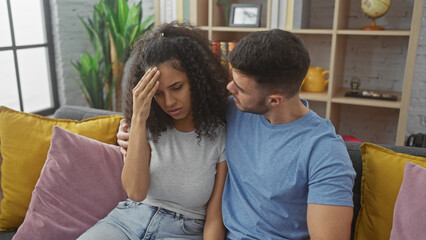 A concerned man comforts a distraught woman on a sofa in a cozy home interior.