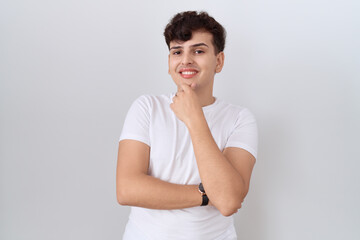 Young non binary man wearing casual white t shirt looking confident at the camera smiling with...