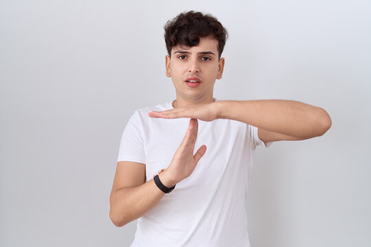 Young non binary man wearing casual white t shirt doing time out gesture with hands, frustrated and serious face