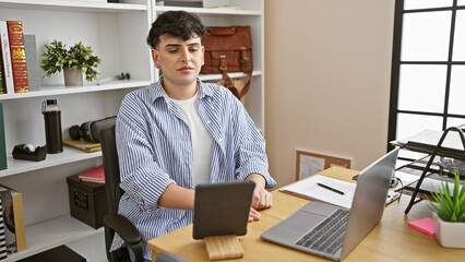 Young man using tablet in a modern office setting, portraying a casual business work environment.