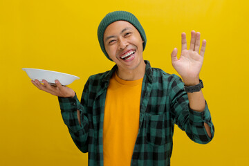 An excited young Asian man, dressed in a beanie hat and casual shirt, cheerfully holds an empty...