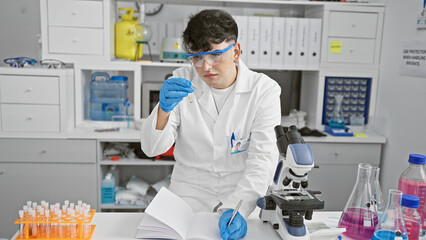 Naklejka premium A focused male scientist analyzes a test tube in a well-equipped laboratory, showcasing research and healthcare.