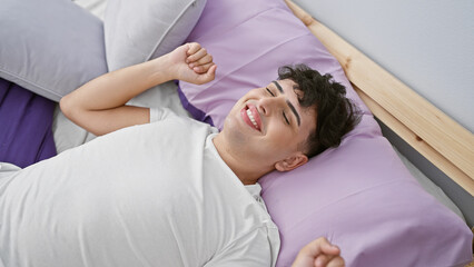 A joyful young man waking up relaxed in a comfortable bedroom setting, expressing happiness and...