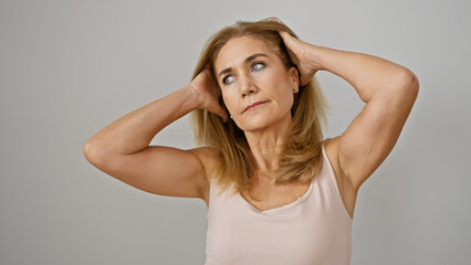 A contemplative blonde woman in a sleeveless top isolated against a white background poses with her...