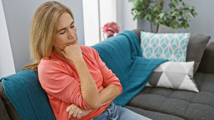 A contemplative middle-aged woman sitting on a blue couch indoors.