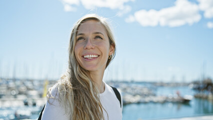 A smiling young blonde woman enjoys a sunny day at a seaside marina, representing beauty and...