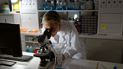 A focused young woman scientist examines samples using a microscope in a well-equipped laboratory.
