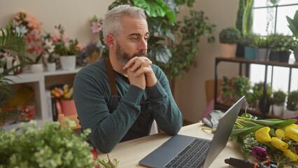 Bearded man in florist shop working on laptop surrounded by plants