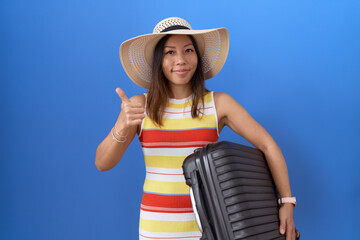 Middle age chinese woman holding suitcase going on summer vacation smiling happy and positive,...