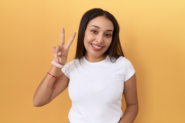 Young arab woman wearing casual white t shirt over yellow background smiling with happy face...