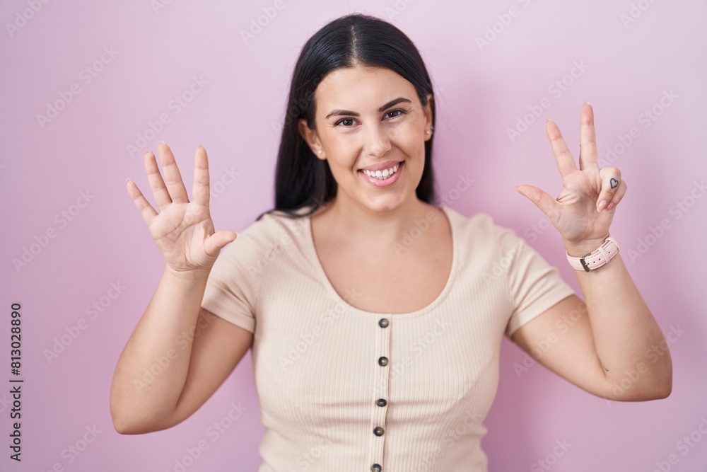 Sticker Young hispanic woman standing over pink background showing and pointing up with fingers number eight while smiling confident and happy.