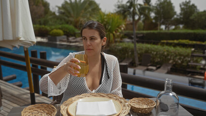 A young woman enjoys a refreshing drink on a tropical resort terrace overlooking a serene pool.