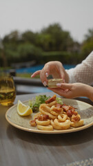 Woman dining outdoors, enjoying calamari and a drink at a restaurant