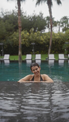 A beautiful brunette woman relaxes in an outdoor bali resort pool, embodying leisure and tropical serenity.