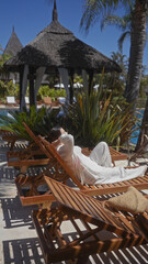 A relaxed woman lounging on a wooden sunbed at a luxurious bali resort, surrounded by tropical vegetation.