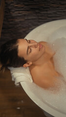 A serene young woman enjoys a relaxing bubble bath in a cozy, wood-accented bathroom.