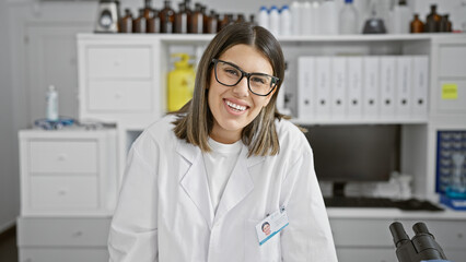 Smiling young hispanic woman medical researcher wearing glasses in laboratory, portrait