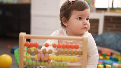 Adorable toddler playing with abacus sitting on floor at kindergarten