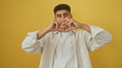 Handsome arab man making heart gesture with hands against yellow isolated background