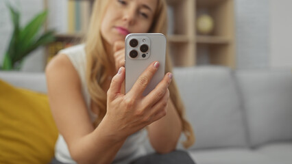 Blonde woman using smartphone on couch at home, showcasing technology and lifestyle.