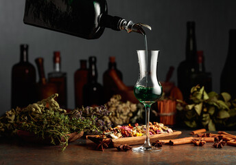 Green herbal liquor is poured from a vintage bottle into a glass.