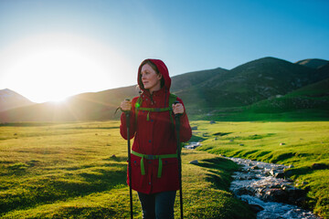 Young woman tourist standing by stream in picturesque mountain valley on a sunny day