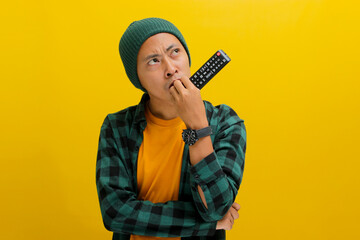 Pensive young Asian man, dressed in a beanie hat and casual shirt, appears puzzled while selecting...