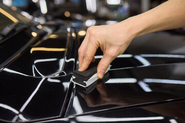 Hand gestures polishing black car hood with sponge